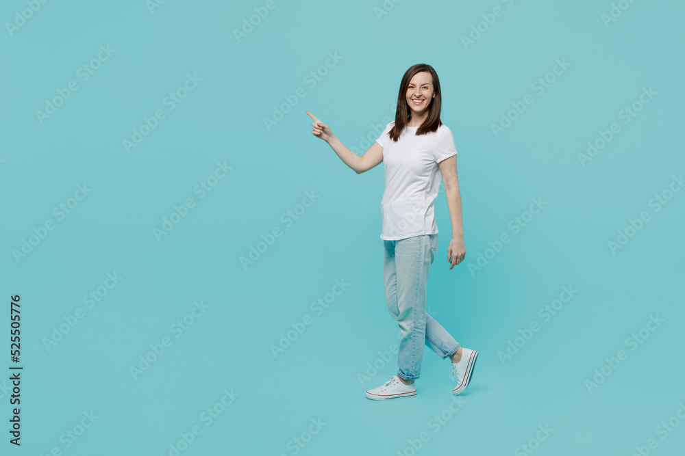 Full body side view young caucasian woman 20s wear white t-shirt walking going strolling point index finger aside on workspace area mock up isolated on plain pastel light blue cyan background studio. Full body side view young caucasian woman 20s wear white t-shirt walking going strolling point index finger aside on workspace area mock up isolated on plain pastel light blue cyan background studio.