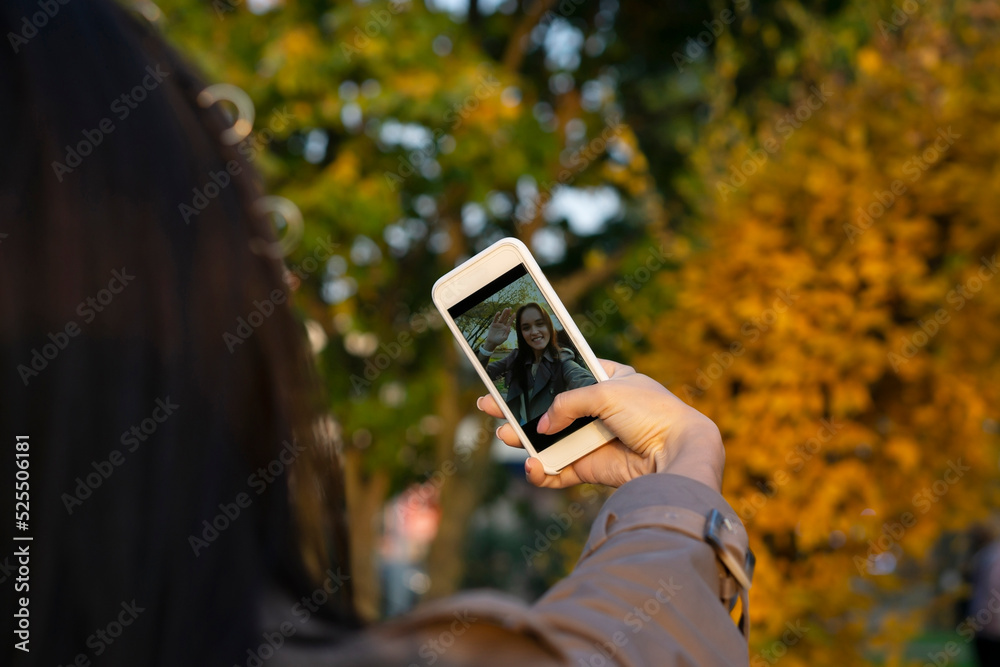 young woman having video chat  using  phone  camera  in the city park