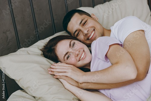 Young smiling happy fun calm lovely caucasian couple two family man woman she he wearing t-shirt pajama lying in bed rest spending time together in bedroom home in own room hotel. Real estate concept. © ViDi Studio