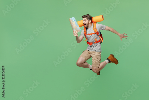 Young fun surprised traveler white man carry backpack stuff mat hold map jump isolated on plain green background Tourist leads active lifestyle walk on spare time Hiking trek rest travel trip concept #525506557