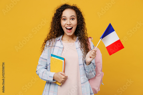 Young surprised excited cool black teen girl student she wearing casual clothes backpack bag hold books french flag isolated on plain yellow color background. High school university college concept. photo