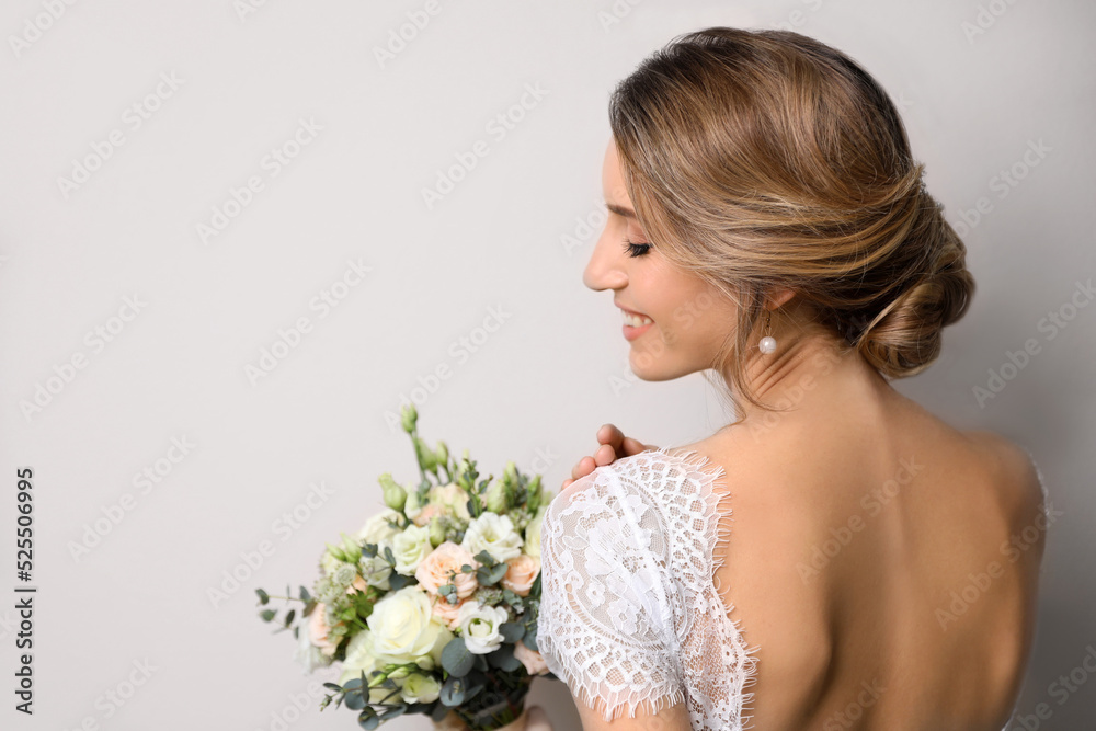 Young bride with elegant hairstyle holding wedding bouquet on beige background