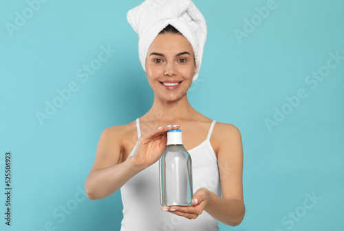 Young woman with bottle of micellar water on light blue background
