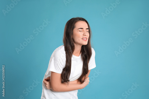 Young woman suffering from stomach ache on light blue background. Food poisoning