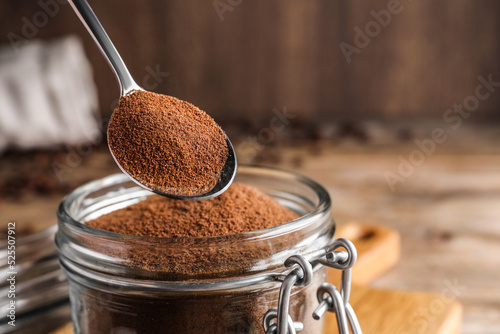 Instant coffee and spoon above glass jar on table, closeup