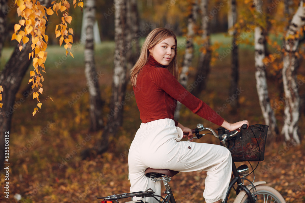 Happy active young beautiful girl riding bicycle at autumn natural parkland.