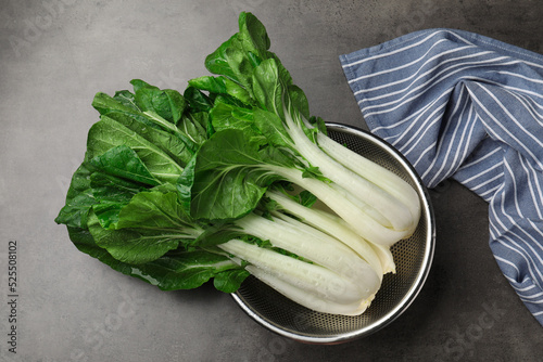 Fresh green pak choy cabbages with water drops in sieve on grey table, top view photo