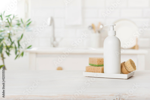 Foto White plastic dishwashing gel bottle with sponges on kitchen table