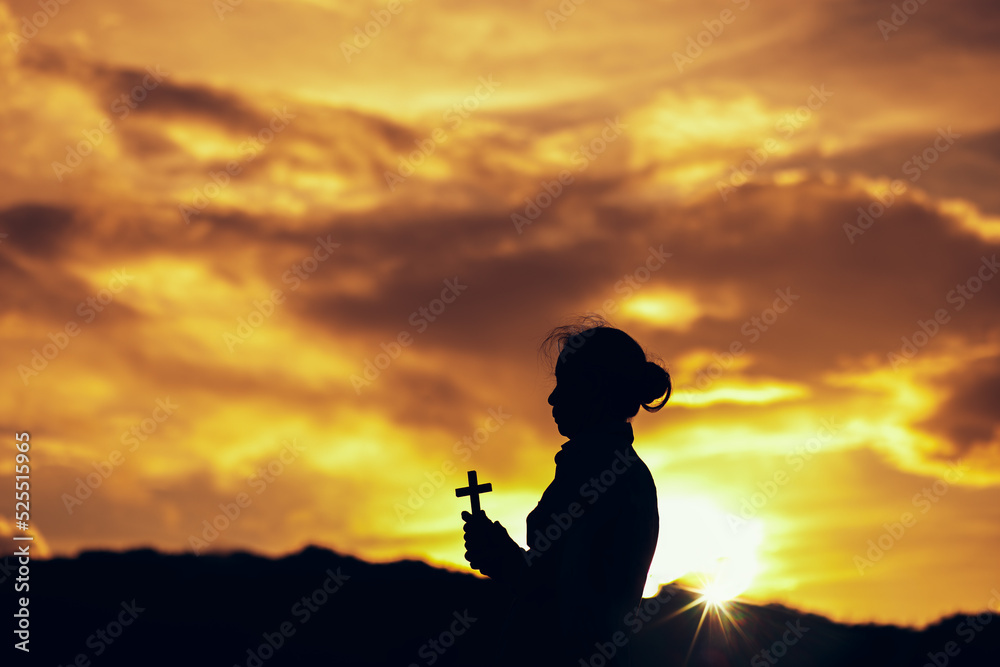 Silhouette of Christian woman praying and worship with holding Cross in hands at sunset. worship to God. Christian Religion concept background. Copy space for your individual text.