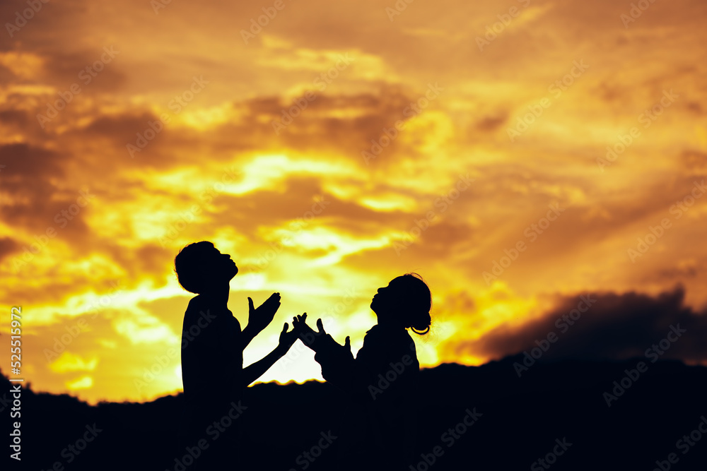 Silhouette of two people praying and worship to God at sunset. Hands in prayer. Christian Religion concept background. Copy space for your individual text.