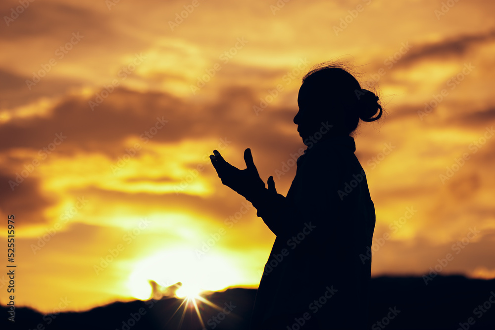 Silhouette of a woman praying and worship to God at sunset. Hands in prayer. Christian Religion concept background. Copy space for your individual text.