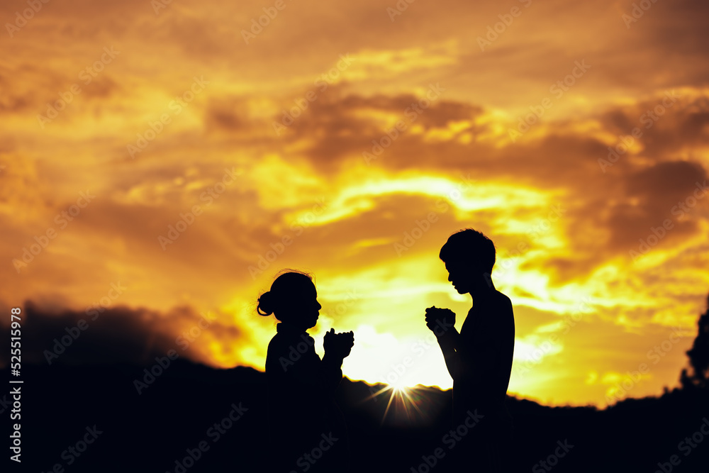 Silhouette of mother and son praying and worship to God at sunset. Hands in prayer. Christian Religion concept background. Copy space for your individual text.