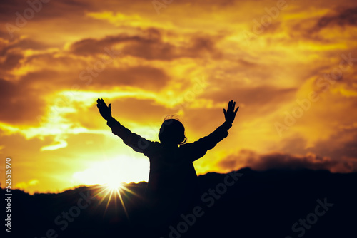 Silhouette of a woman raised hands praying and worship to God at sunset. Christian Religion concept background. Copy space for your individual text.