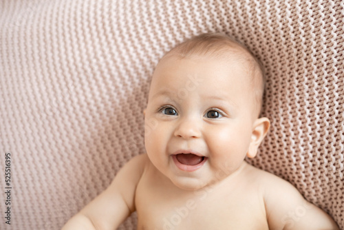 Funny portrait of a baby on a pink knitted plaid. Lifestyle. Light background. Space for text.