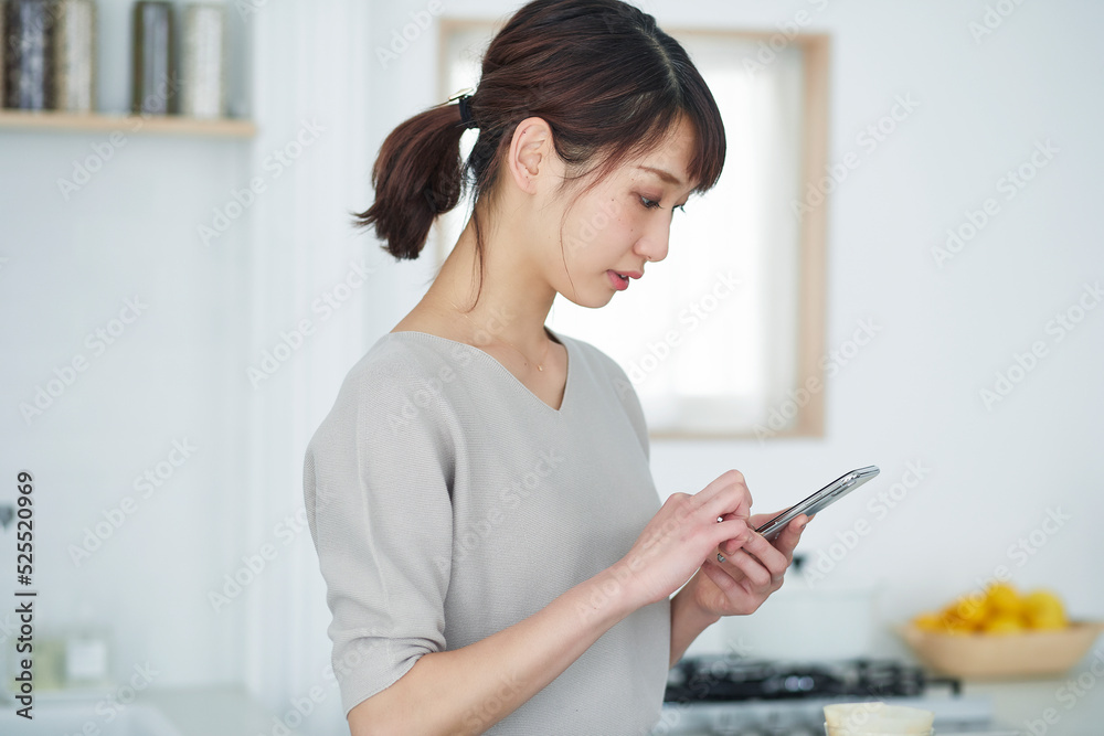 キッチンでスマートフォンを操作する女性 キッチンでスマートフォンを操作する女性