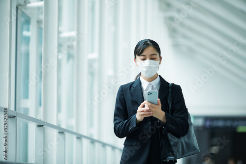 マスクをしながらスマートフォンを持つスーツを着た若い女性 photo