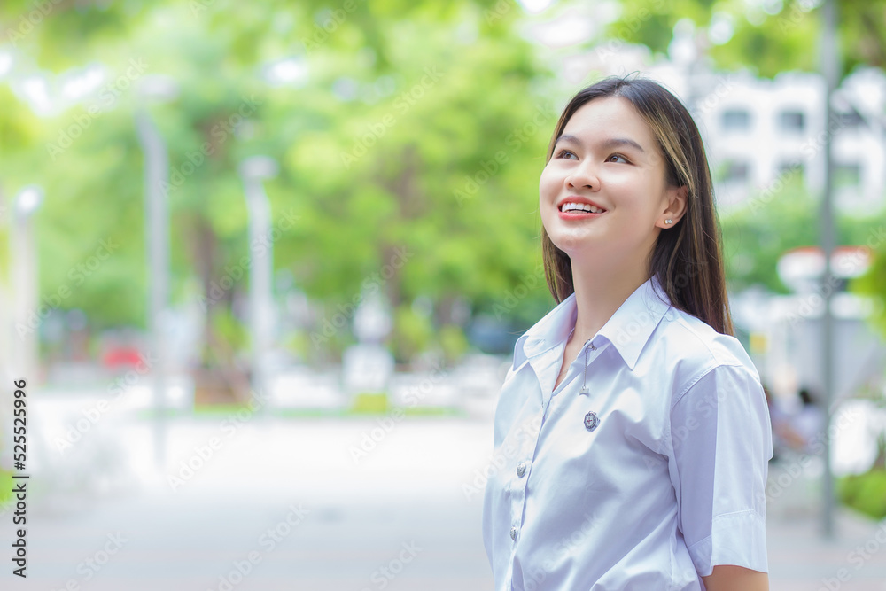 Portrait of adult Thai student in university student uniform. Asian beautiful girl standing smiling confidence at outdoors university with a background of outdoors garden trees. Portrait of adult Thai student in university student uniform. Asian beautiful girl standing smiling confidence at outdoors university with a background of outdoors garden trees.