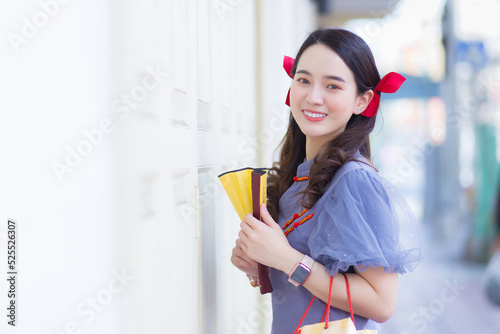 Asian beautiful woman in a gray Qipao dress with a red bow is smiling, holding a fan on the street in Chinatown, Thailand.