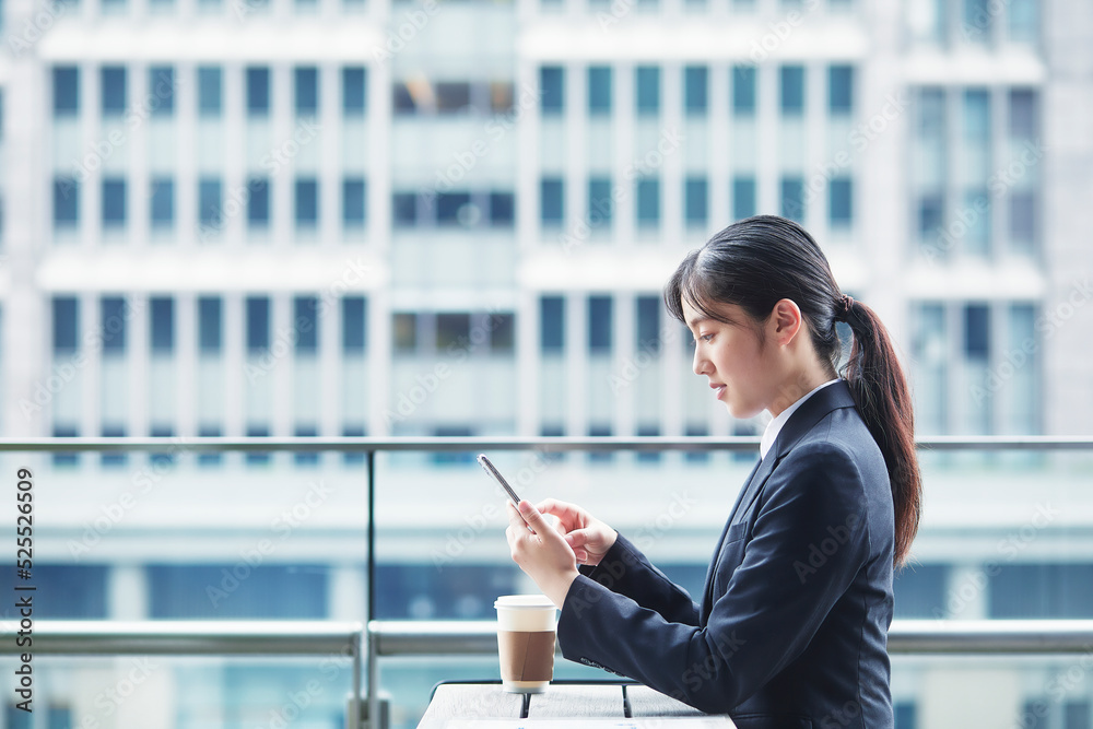 オフィス街のカフェでスーツを着てスマートフォンを持つ若い女性
