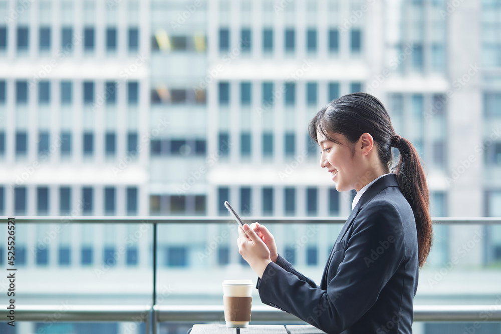 オフィス街のカフェでスーツを着てスマートフォンを持つ若い女性 オフィス街のカフェでスーツを着てスマートフォンを持つ若い女性