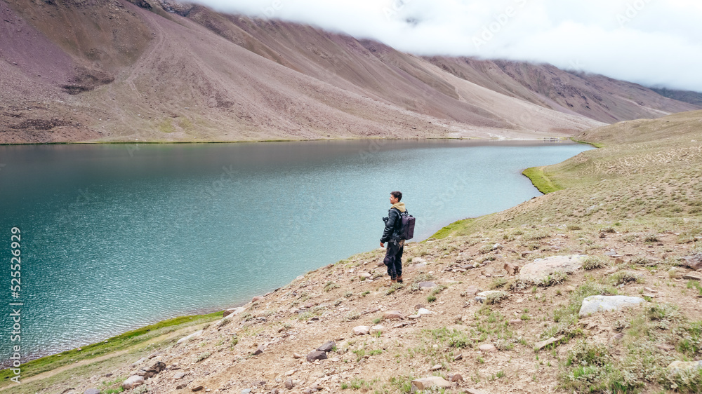 male tourist standing at Chandra Taal Lake overlooking blue glacier water in Spiti Valley India on cloudy day