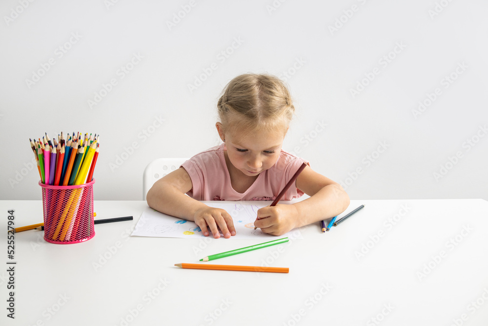 Blonde child girl draws with colored pencils sitting at the table Blonde child girl draws with colored pencils sitting at the table