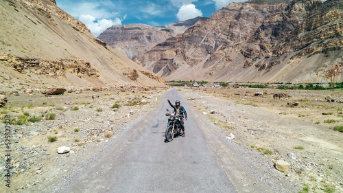 Man on touring motorcycle adventure through Spiti Valley India on sunny summer day surrounded by extreme mountains