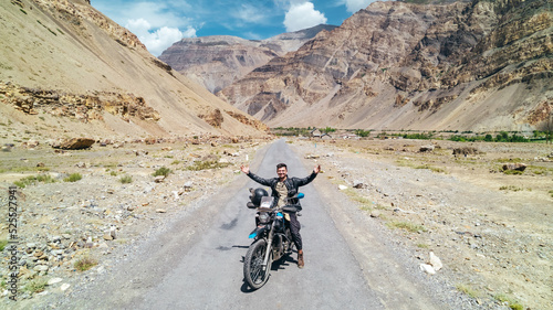 excited man on motorcycle adventure with incredible Himalayan Mountain landscape in Spiti Valley India