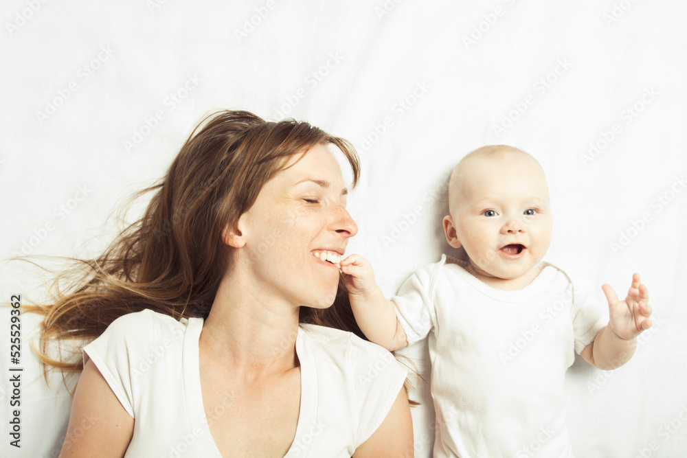 Young mother plays with her baby on a bed with a white sheet. Flat lay, top view Young mother plays with her baby on a bed with a white sheet. Flat lay, top view