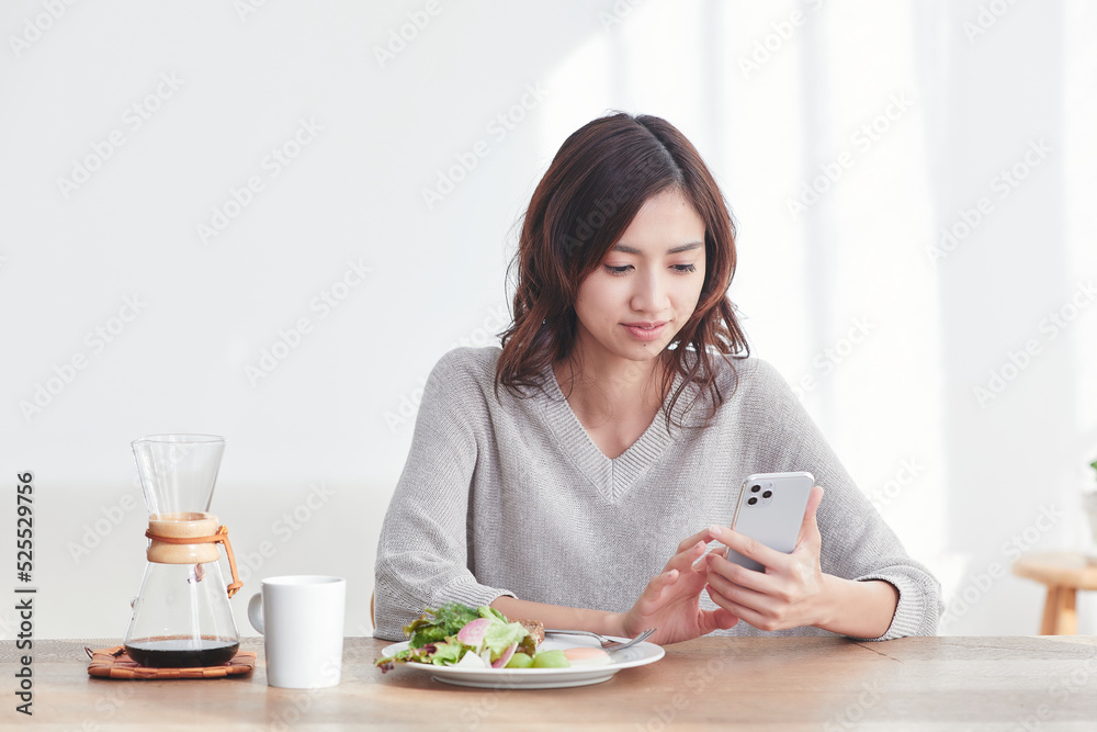 スマホを見ながら食事をする若い日本人女性 スマホを見ながら食事をする若い日本人女性