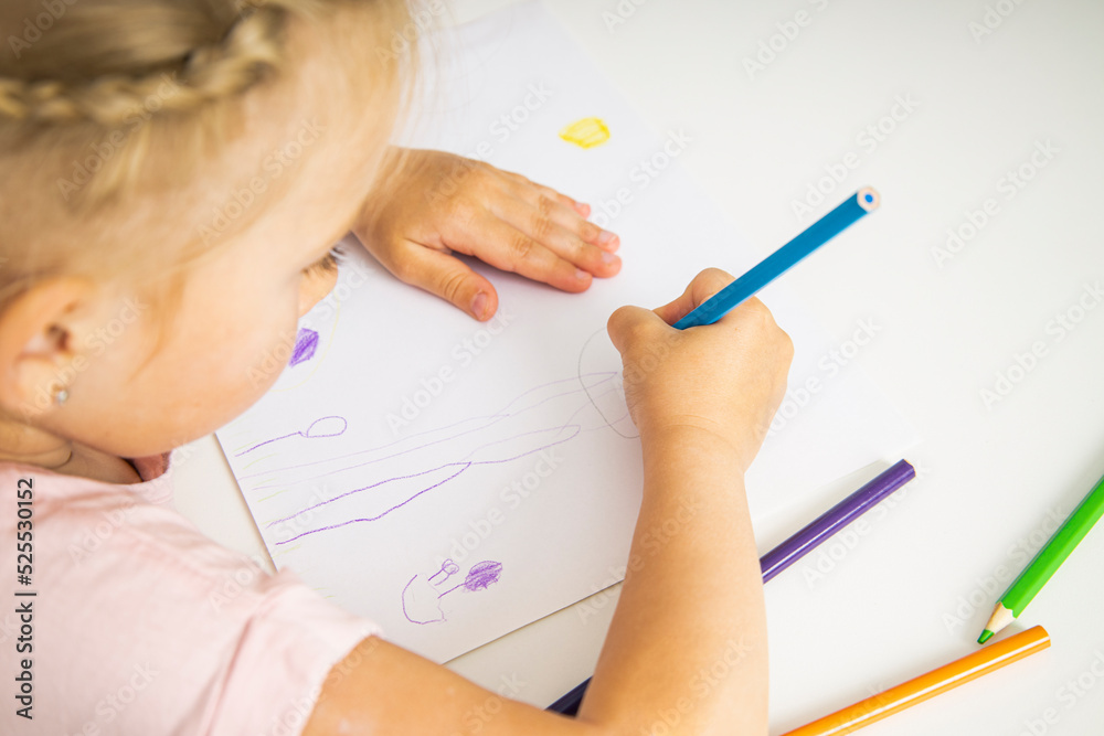 A child blonde girl draws with colored pencils sitting at the table A child blonde girl draws with colored pencils sitting at the table