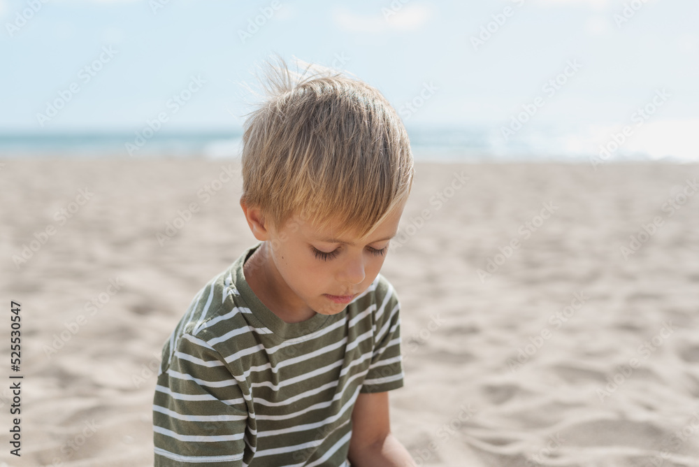 Candid portrait of a pensive little boy sitting on a sandy beach Candid portrait of a pensive little boy sitting on a sandy beach