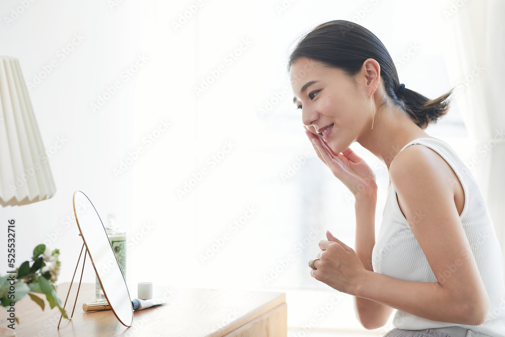 部屋で鏡を見ながらスキンケアをする女性