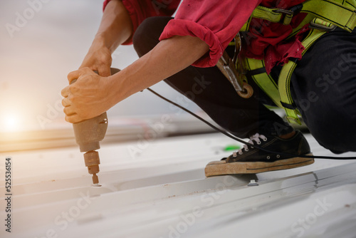 Construction workers work installing new roofs on houses and buildings. Use an electric drill to install the roof as a roofing tool.