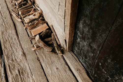 A pile of logs in front of a door at a wooden house. Timber porch outdoor detail. Old house with chopped firewood. © Moodlia