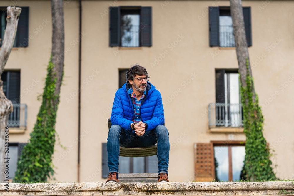 Middle-aged man sitting on a wooden chair while pensively Middle-aged man sitting on a wooden chair while pensively
