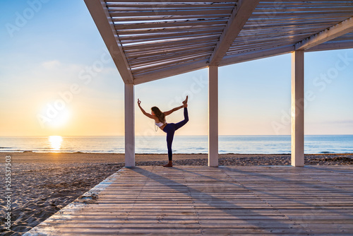 Woman doing yoga in standing split pose at seaside photo