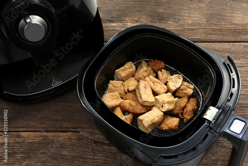 homemade fry tofu and fry taro are cooked by using a black air fryer or oil free fryer appliance for being lunch in afternoon party with background of old vintage wooden table in the dinning room. photo