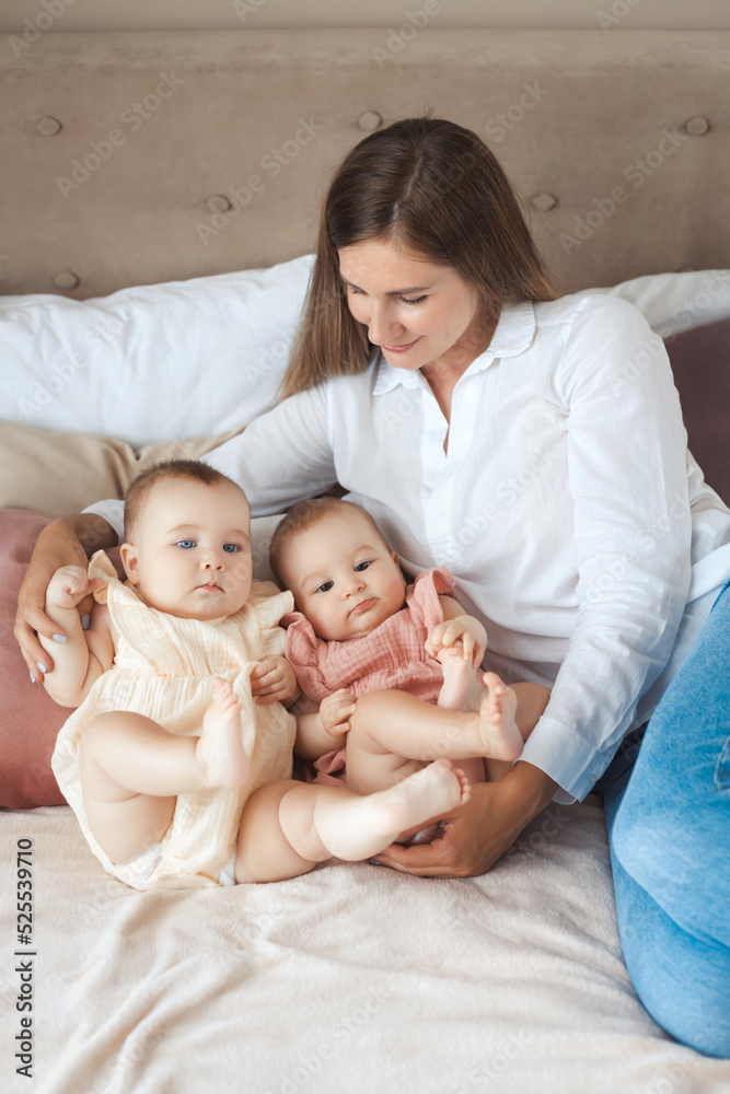 Portrait of young happy mother take care after two little twin daughters, lying together on a soft bed at home Portrait of young happy mother take care after two little twin daughters, lying together on a soft bed at home