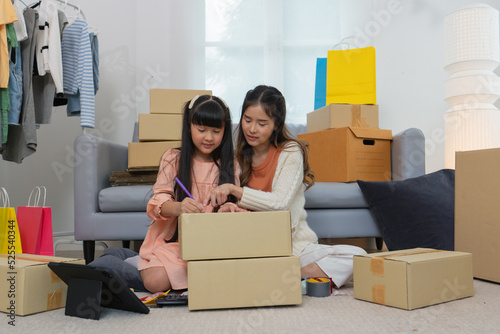 Mother and daughther as team working from home social live chat online sale business via computer tablet pc and show sample cloth and size meassurement before packing to the box and seal adhesive tape photo