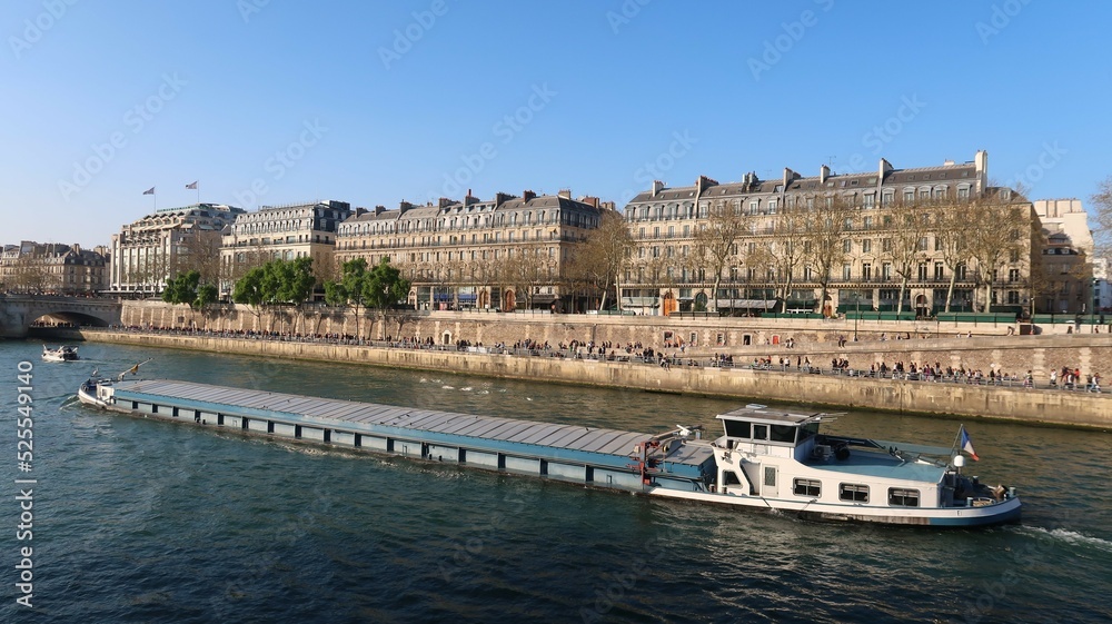 Transport fluvial de marchandises par péniche sur la Seine, dans la ville de Paris, avec des immeubles haussmanniens bordant le fleuve, quai de la Mégisserie (France)
