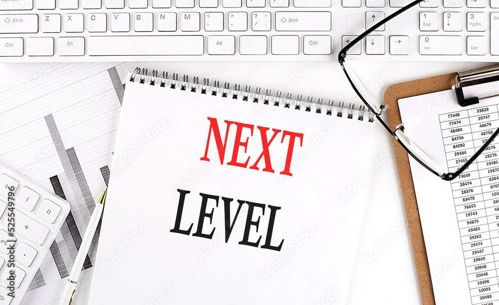 Text NEXT LEVEL on Office desk table with keyboard, notepad and analysis chart on white background. Text NEXT LEVEL on Office desk table with keyboard, notepad and analysis chart on white background.