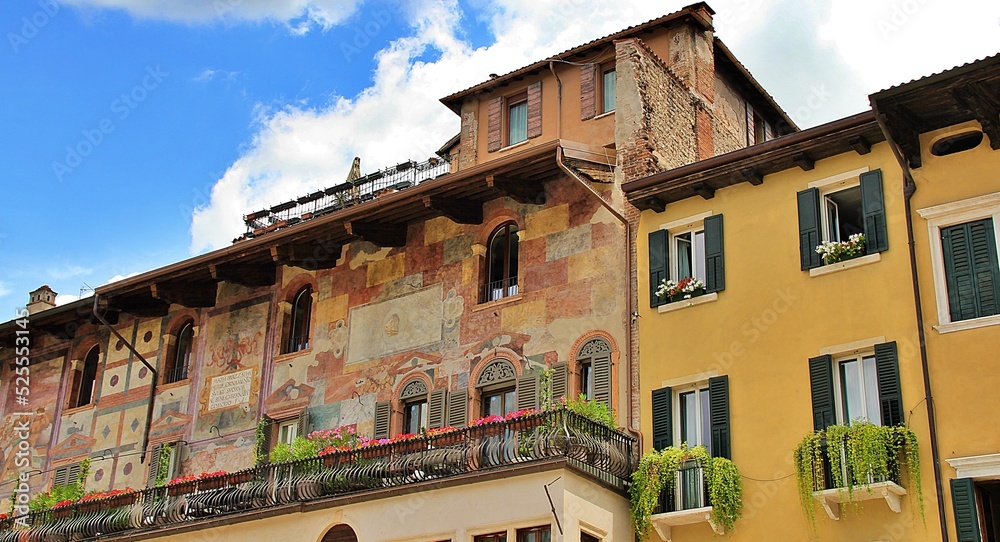 Italian architecture, Verona architecture, blue sky with white clouds, wooden shutters and greenery on balconies, paintings on the facade of a tenement house