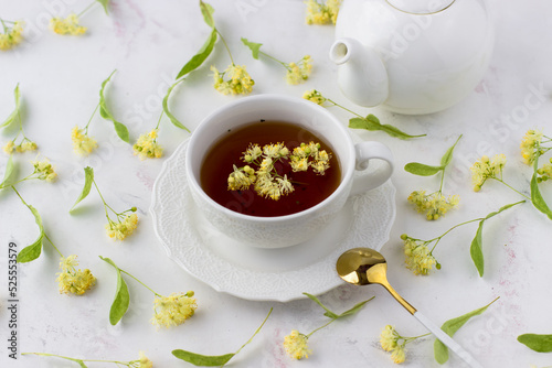 Tea with linden in a white cup on a white marble table. White teapot with aromatic tea