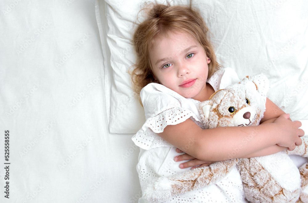 Child girl in bed holding toy empty white copy space.Little girl top view portrait. Caucasian kid health care and hygiene concept.