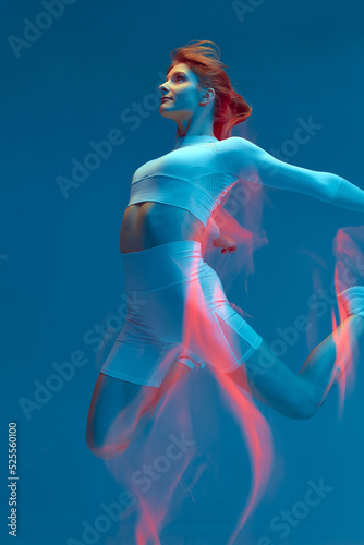 Jumping fitness girl on blue. Sportive woman jumps in air. Long exposure, motion blur. Freedom, sports lifestyle
