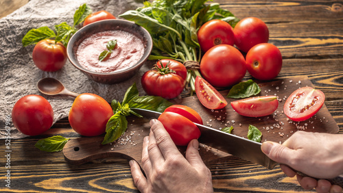 Hand is slicing ripe natural homemade tomatoes to make tomato basilic sauce. Rustic style