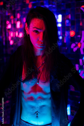 Portrait of a transgender model with a naked torso in a studio with neon lighting.