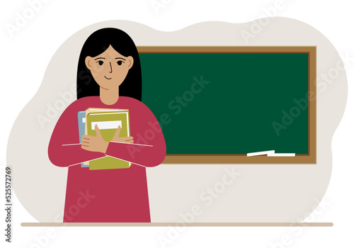 Female teacher with books on the background of the school board.