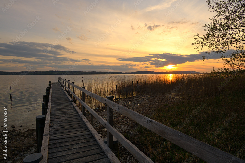 Abendrot an einem See, in den ein Bootssteg aus Holz führt.